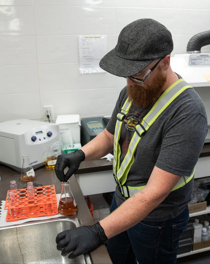 Person in a laboratory setting wearing safety gear and working with beakers.